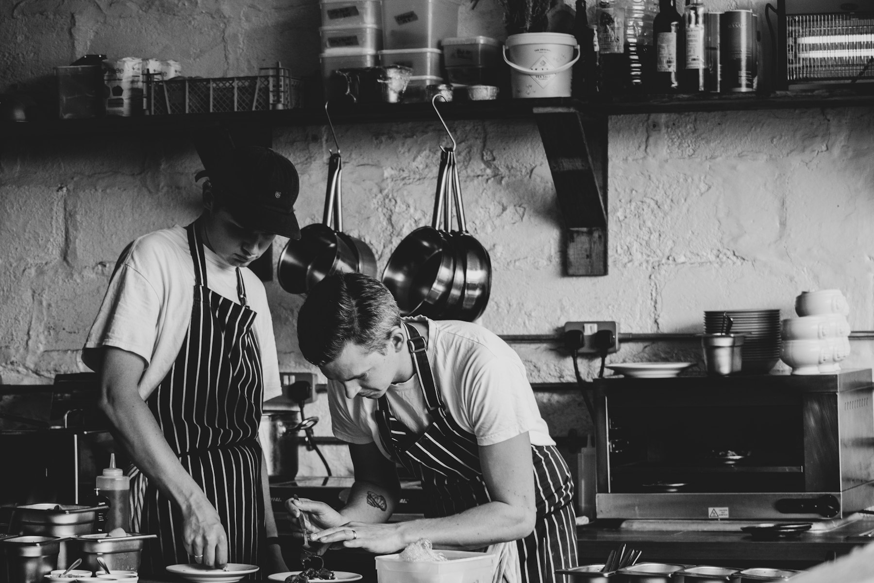 Deux cuisiniers en tablier au travail dans une cuisine, noir et blanc